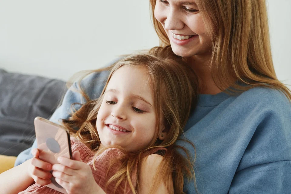 A child and adult looking at a phone together on a sofa