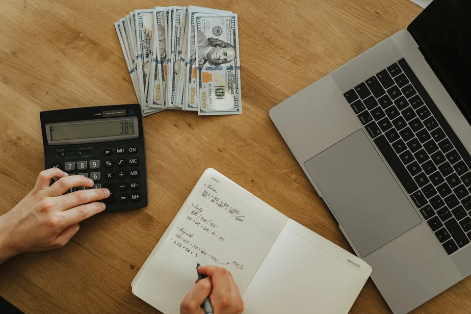 Hands using a calculator beside a notebook and banknotes