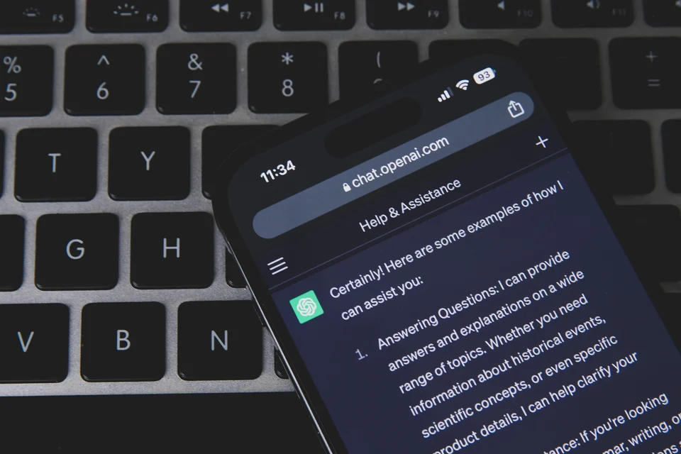 A smartphone showing the ChatGPT chat screen lies on a laptop keyboard
